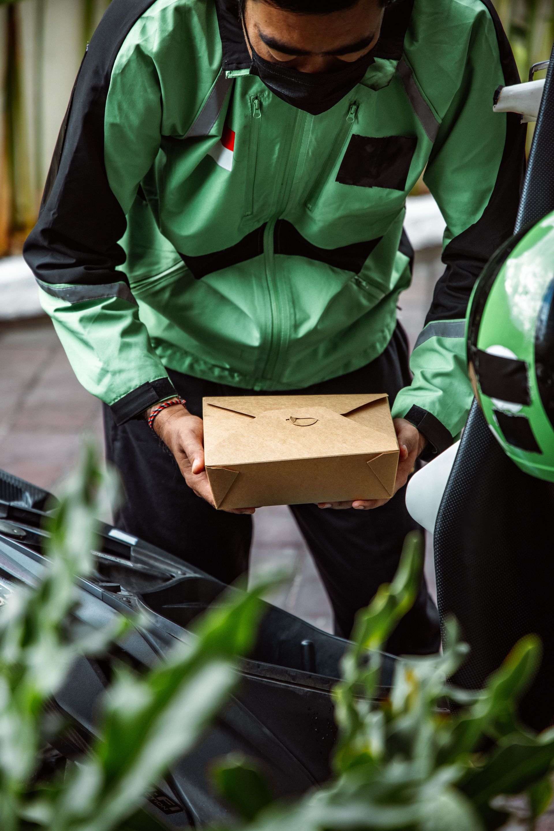 Courier in green uniform holding a package near a scooter